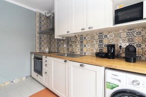 A kitchen with white cabinets, a wooden countertop, a microwave, a coffee maker, and a washing machine.