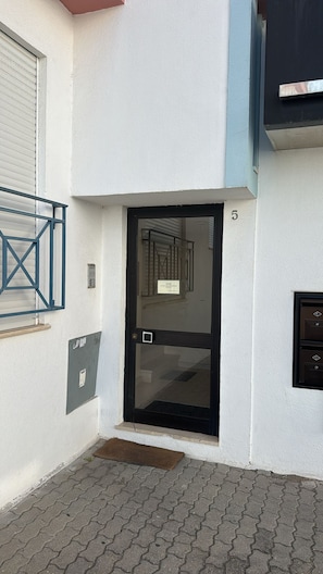 A modern building entrance with a glass door, a metal gate, and a small step leading up to the door.