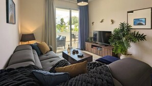 Een moderne woonkamer met een bank, salontafel, televisie en een balkon met gordijnen.