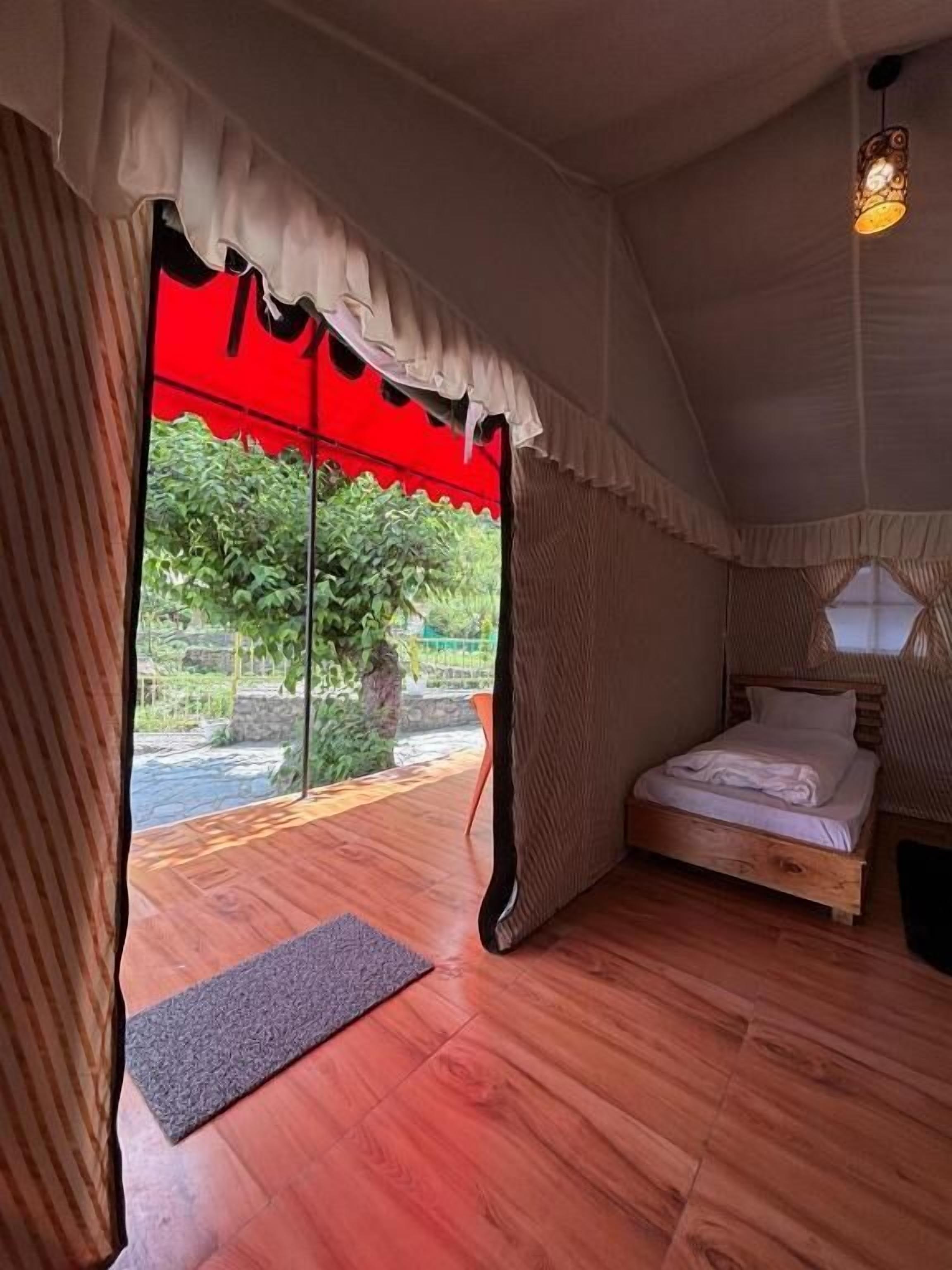 A tent-style room with a bed, a small rug, and a view of greenery outside.