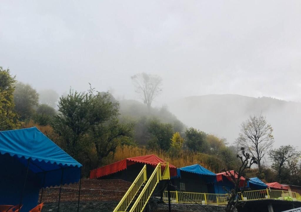 A series of tents with steps leading up to them, set in a foggy, hilly area with trees in the background.