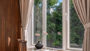 A wooden desk with a chair, a vase with flowers, and a window with curtains.