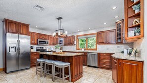 Una cocina amplia con gabinetes de madera, electrodomésticos de acero inoxidable y una isla grande con taburetes de bar.