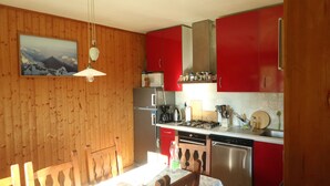 A kitchen with wooden walls, red cabinets, a stainless steel refrigerator, a gas stove, and a microwave.