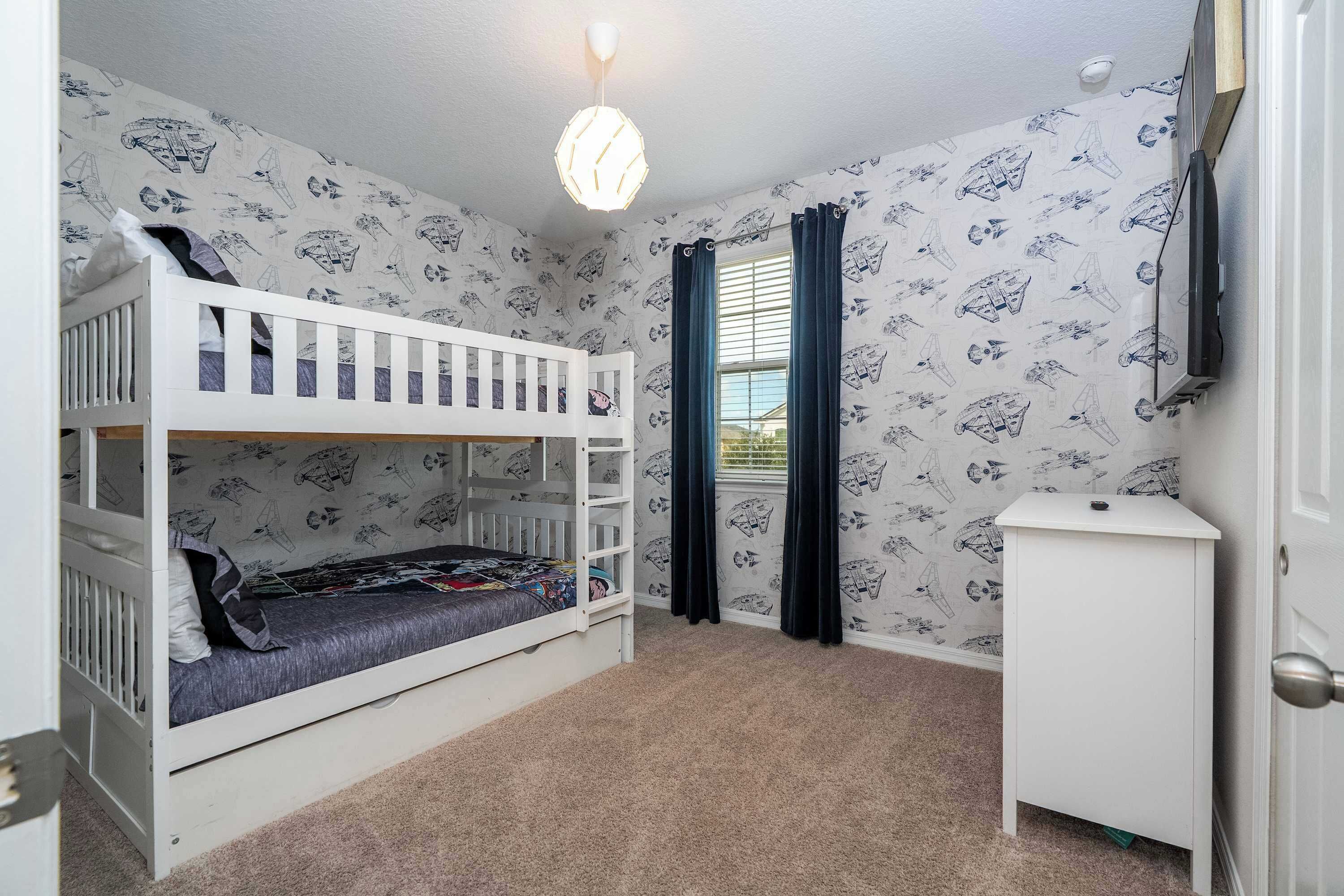 Een kamer met een stapelbed, een klein wit kastje en behang met een patroon.