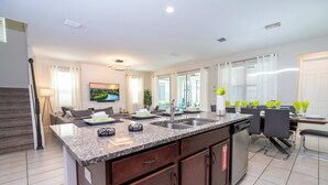 A modern kitchen with granite countertops, a built-in dishwasher, and a dining area with a table and chairs. - Stunning 4Bd w Pool Gameroom Solara Resort 9008 (Kissimmee)