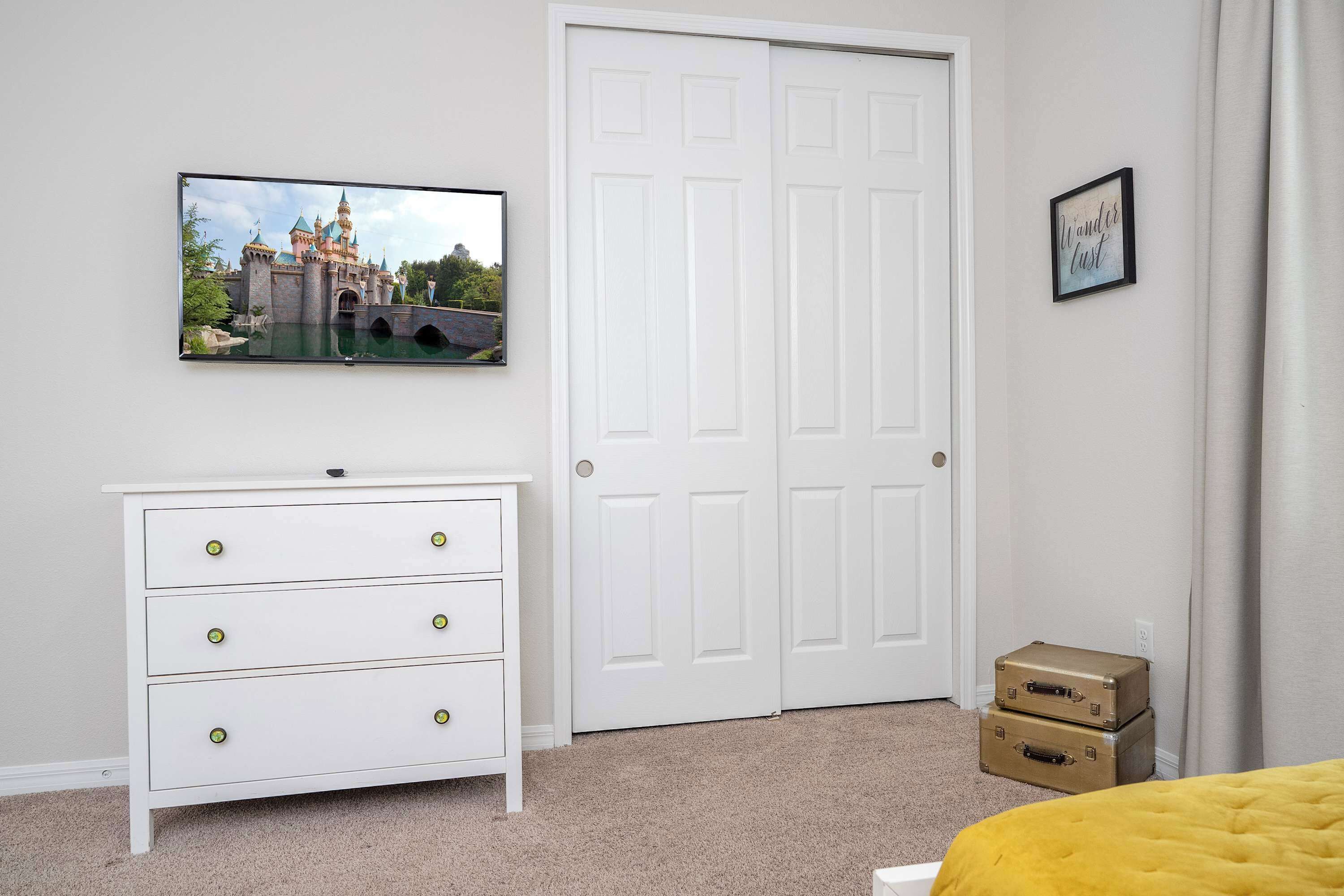 Ein Schlafzimmer mit einem weißen Schminktisch, einem darüber montierten Fernseher, einer weißen Tür und einem gerahmten Schild an der Wand.