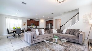 A modern living room with a sectional sofa, a glass coffee table, and a dining area with a table and chairs. - Stunning 4Bd w Pool Gameroom Solara Resort 9008 (Kissimmee)