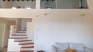 A modern interior with a staircase leading to a second floor, a sofa with striped cushions, and a glass railing on the upper level.