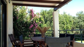 A covered patio with a table and chairs, surrounded by greenery and trees.