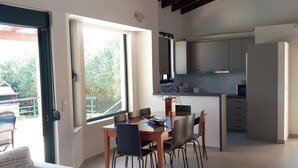 A modern living room with a dining area, kitchen, and large windows.