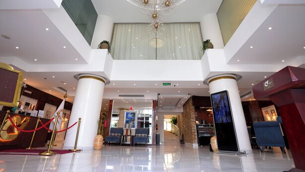 Rebedor d'hotel amb un candelabrum, taulell d'adreça, zona de seients i una escala que condueix a un altre pis.