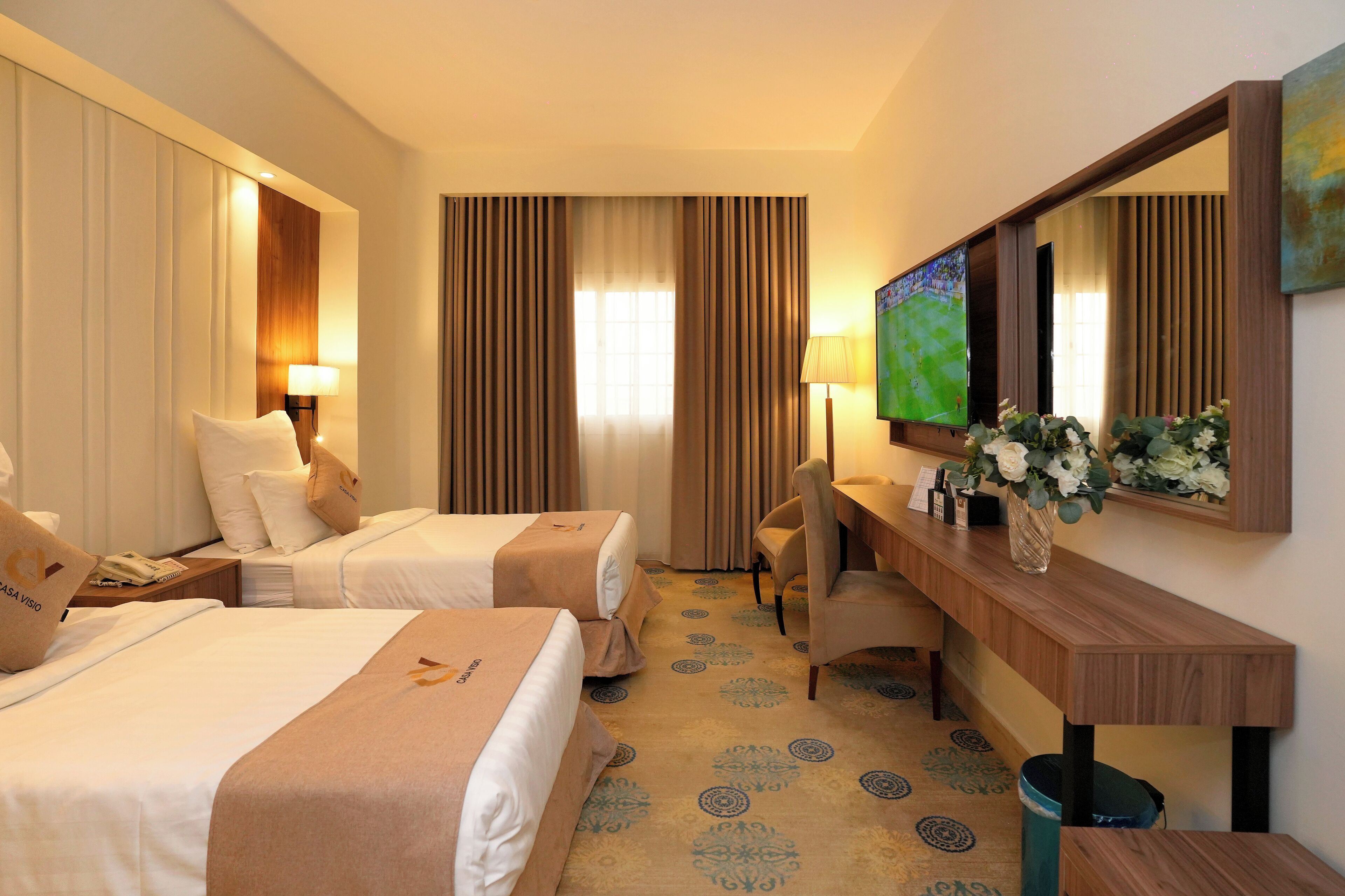 A hotel room with two beds, a desk with a chair, a TV, and a large mirror.