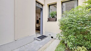 Une entrée étroite avec une porte donnant sur une pièce, une petite fenêtre avec une plante et une plante en pot placée à côté de la porte.