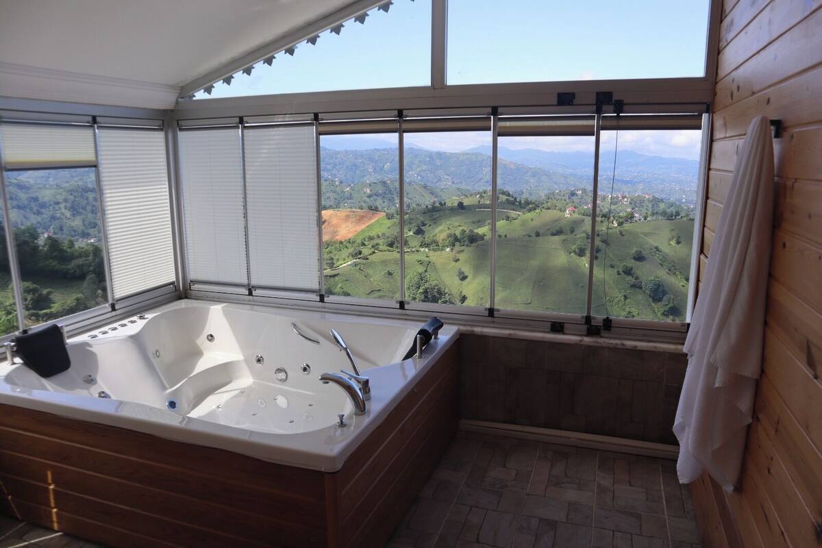 Une salle de bain dotée d’une grande baignoire, d’un plancher en bois et offrant une vue sur un paysage verdoyant grâce à de grandes fenêtres.