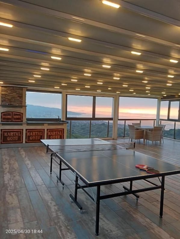 Una mesa de ping pong en una habitación amplia con vistas a montañas al atardecer.