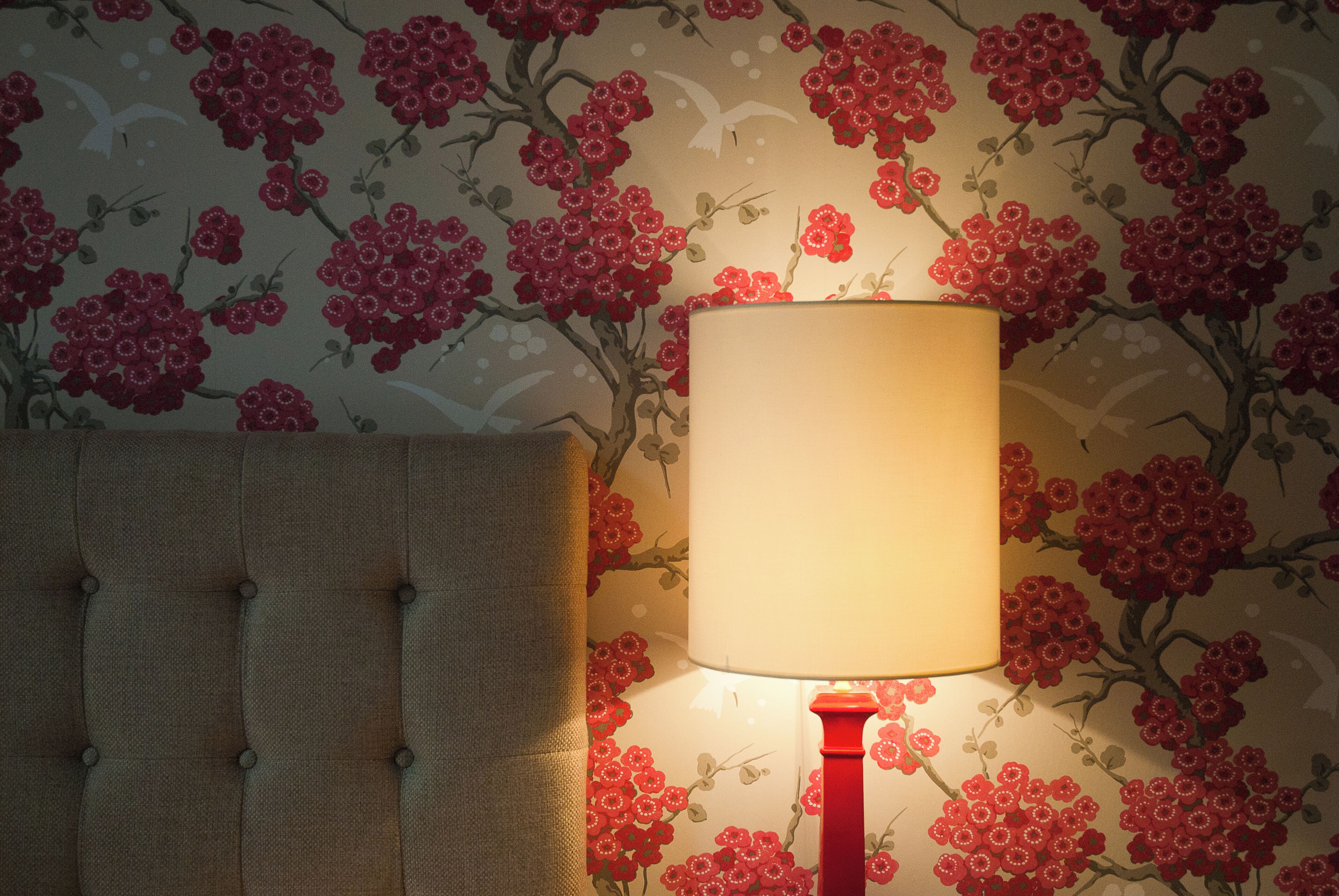 A room with a tufted headboard, a red floor lamp, and floral wallpaper.