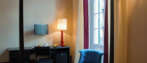 A hotel room with a bed, a desk with a chair, a television, a lamp, and a window with curtains.
