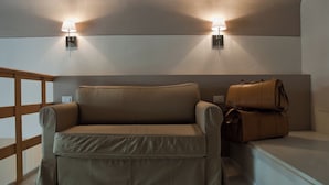 Una habitación con un sofá beige, dos lámparas fijadas a la pared y una barandilla de madera.