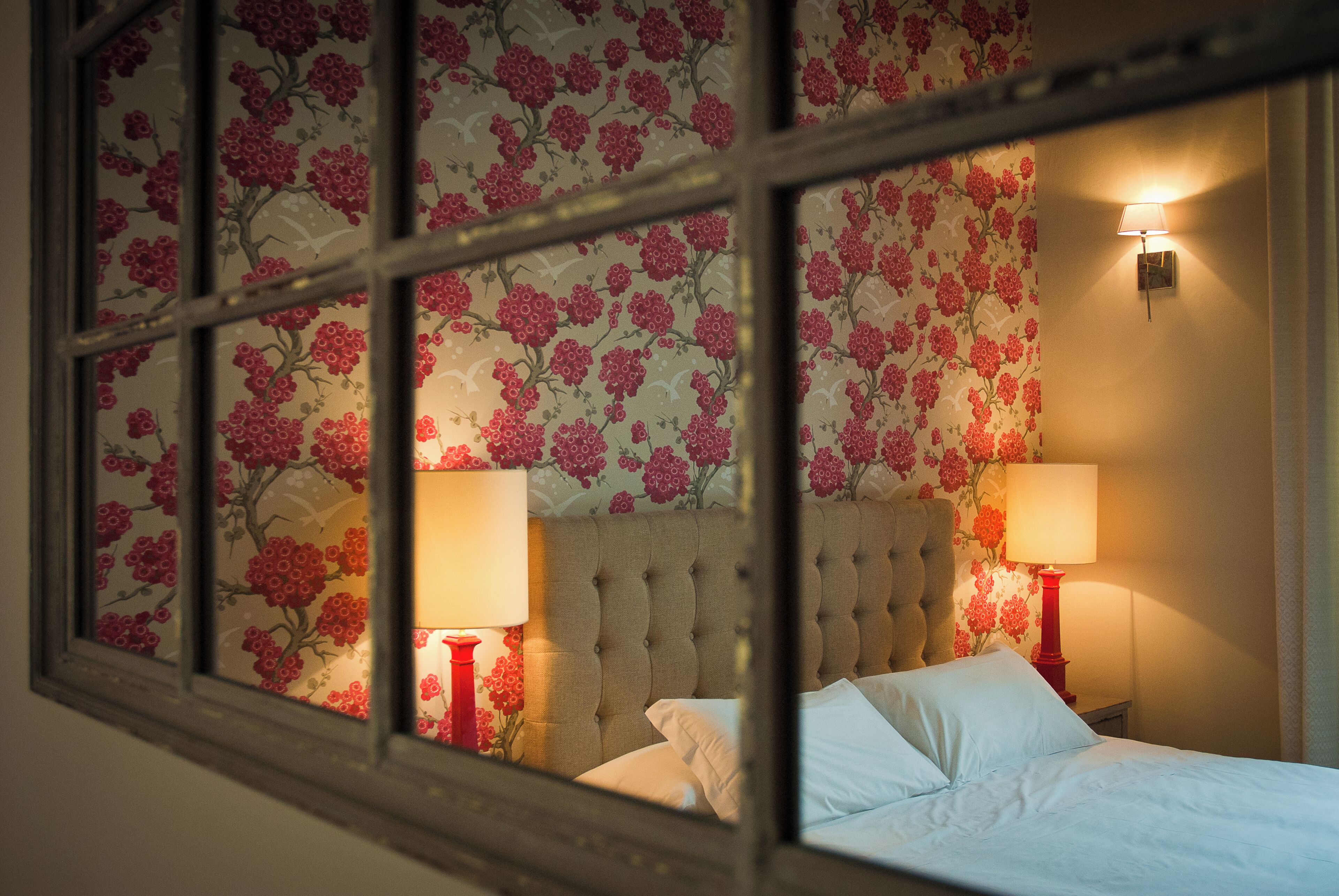 A bedroom with a tufted headboard, two bedside lamps, and floral wallpaper.