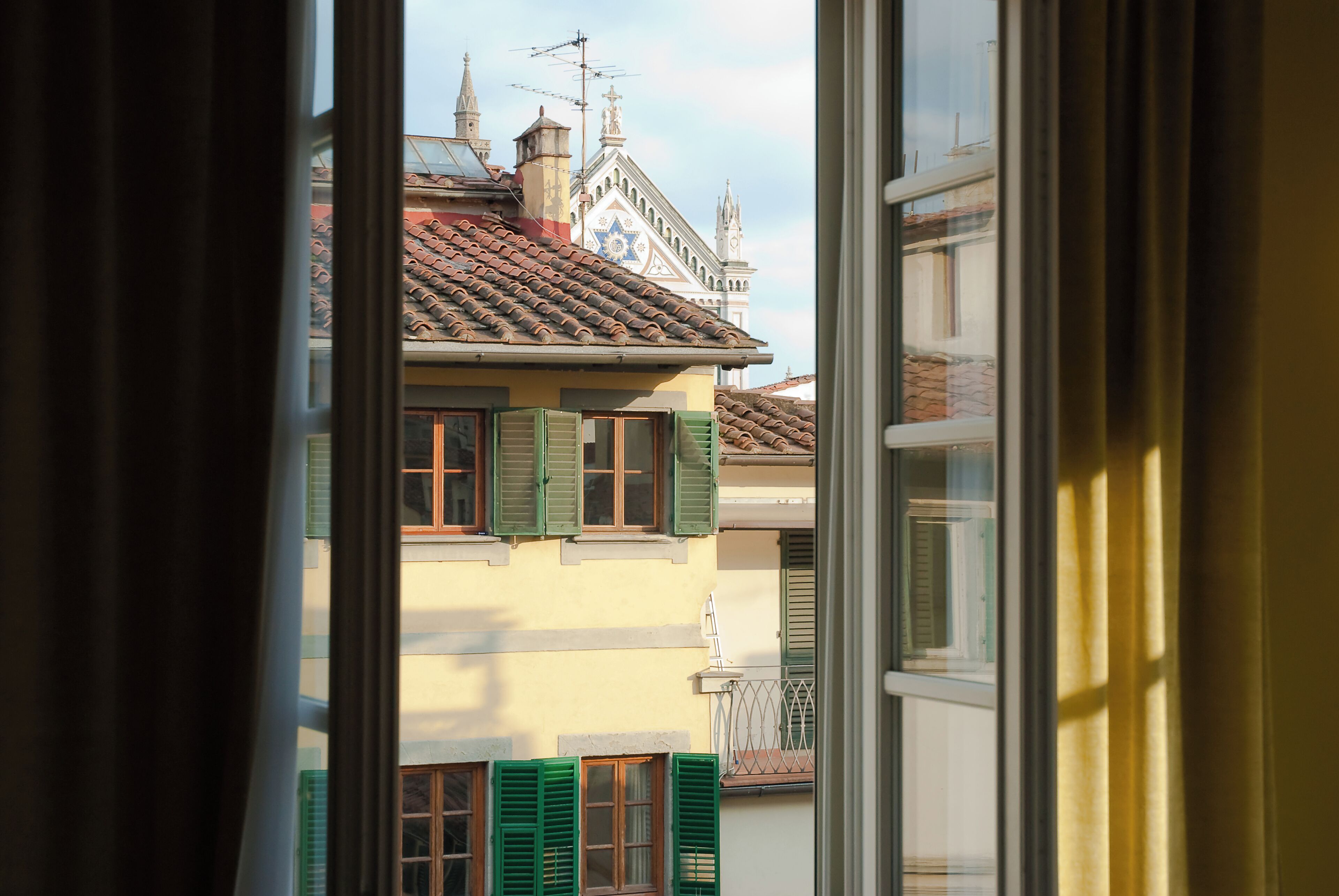 A view through a window of a building with a tiled roof, green shutters, and a star-shaped window.