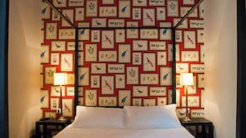 A hotel room with a large bed, two bedside tables, and a wall decorated with framed bird and plant illustrations.