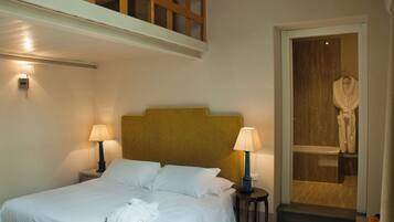 A hotel room with a bed, two bedside lamps, a robe hanging on a door, and a staircase leading to an upper level.