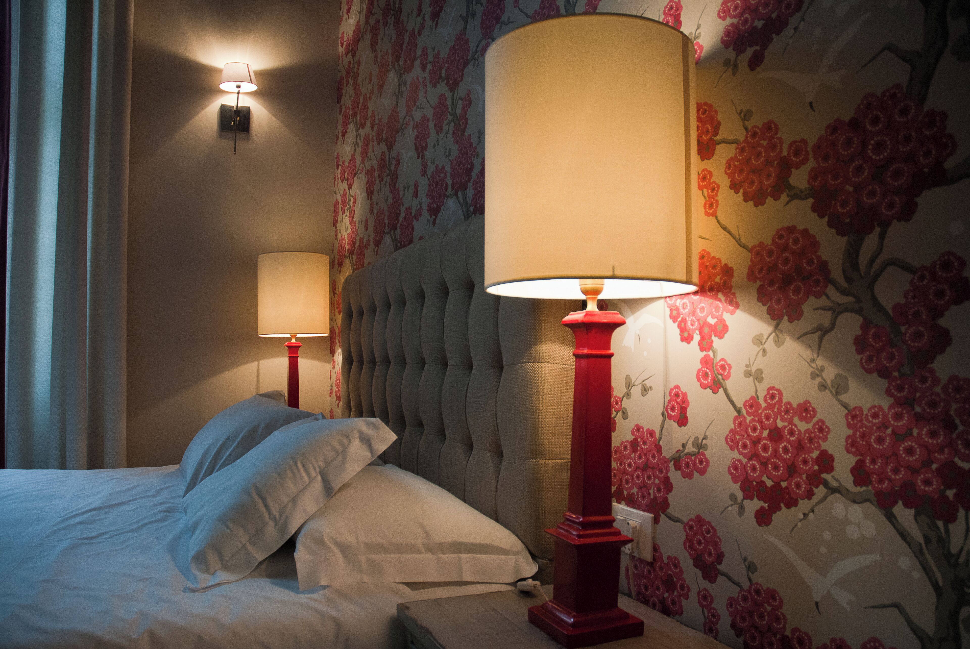 A hotel room with a bed, two bedside lamps, and floral wallpaper.