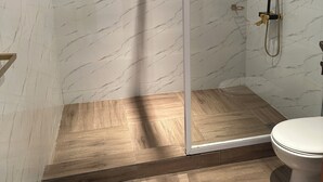 A modern bathroom with a glass-enclosed shower, marble walls, and wooden flooring.