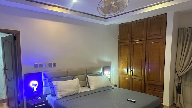 A bedroom with a bed, nightstands, a wooden wardrobe, and a ceiling fan.