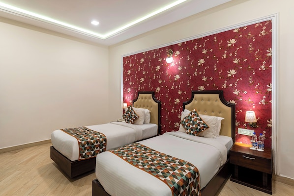 A hotel room with two beds, a nightstand, and a red floral wallpaper. - The Colonial Hotel Lake View Rooms (Udaipur)