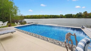 Una piscina rectangular con muelle de madera y sillas de descanso.