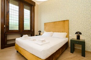 A neatly made bed with white linens and folded towels, a wooden headboard, and a nightstand with a lamp. - Tuscan Refined Retreat (Firenze)