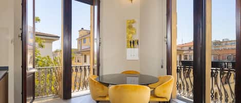 A dining area with a round table and yellow chairs, large windows with a view of buildings, and a wall-mounted light fixture.