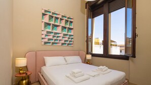 A hotel room with a bed, pillows, a wall art piece, a window, and a nightstand with a lamp. - Tuscan Refined Retreat (Firenze)