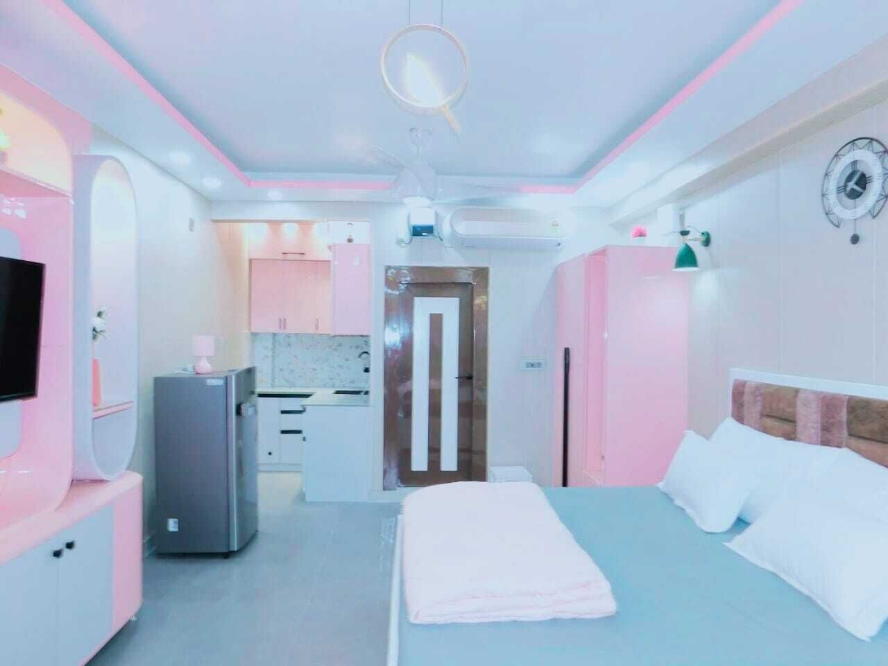 A modern hotel room with a bed, a TV, a refrigerator, and a kitchenette.