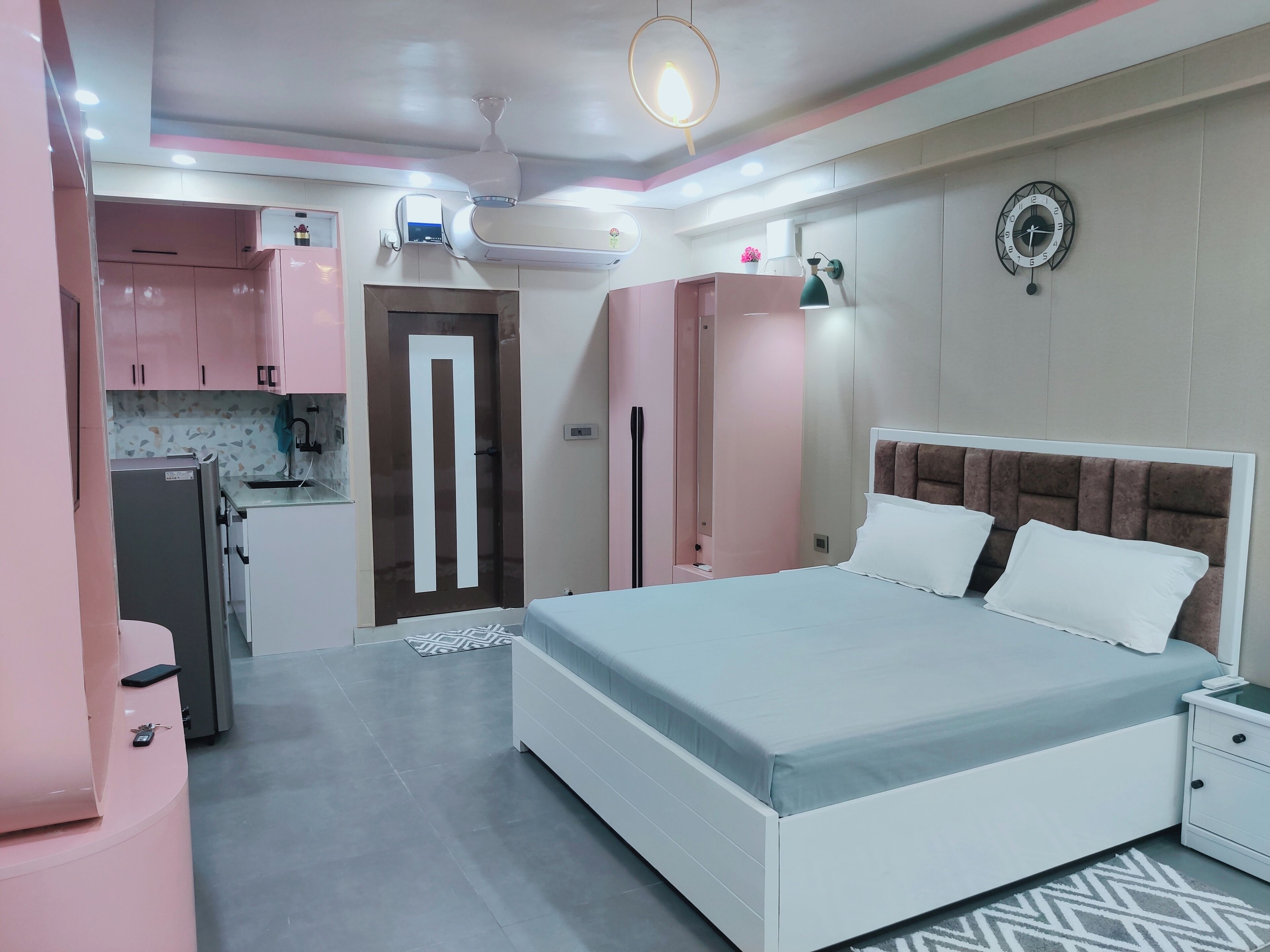 A modern bedroom with a large bed, bedside tables, a wardrobe, and a kitchenette.