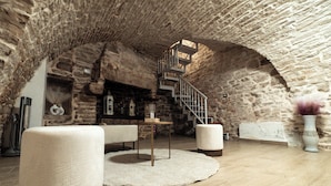 A rustic stone interior with a staircase, a round table, and a white pouf.