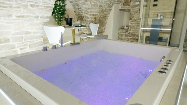 A spa room with a stone wall, a white chair, a massage table, and a bathtub.