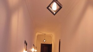 Un pasillo estrecho con piso pulido, una puerta al final e lámparas colgantes en las paredes.