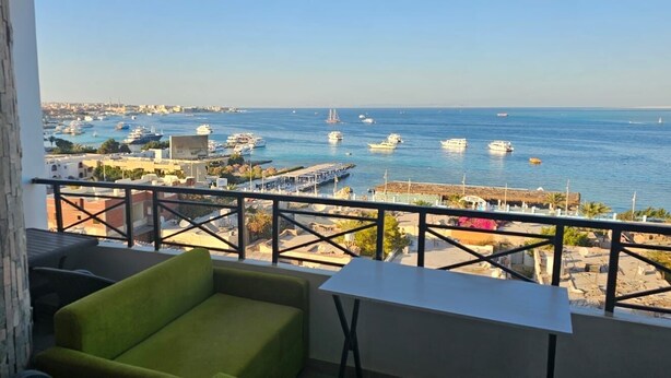 Un balcón con vistas al mar y barcos, un sofá verde y una mesita.