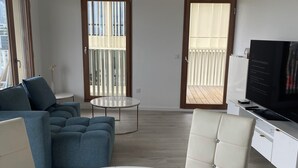 A modern living room with a sofa set, a round coffee table, a dining table, and a TV on a white cabinet.