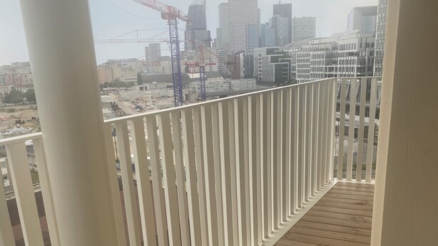 A wooden deck with white railings overlooking a cityscape with modern buildings and construction cranes.
