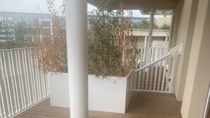 A wooden deck with a white railing, a white pillar, and a view of buildings in the background.
