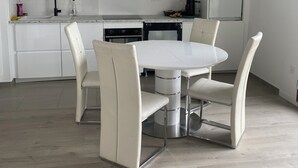 A modern kitchen with white cabinets, a built-in oven, and a dining area with a white table and chairs.