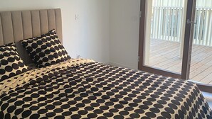 A bedroom with a bed, a headboard, and a view of an outdoor balcony.