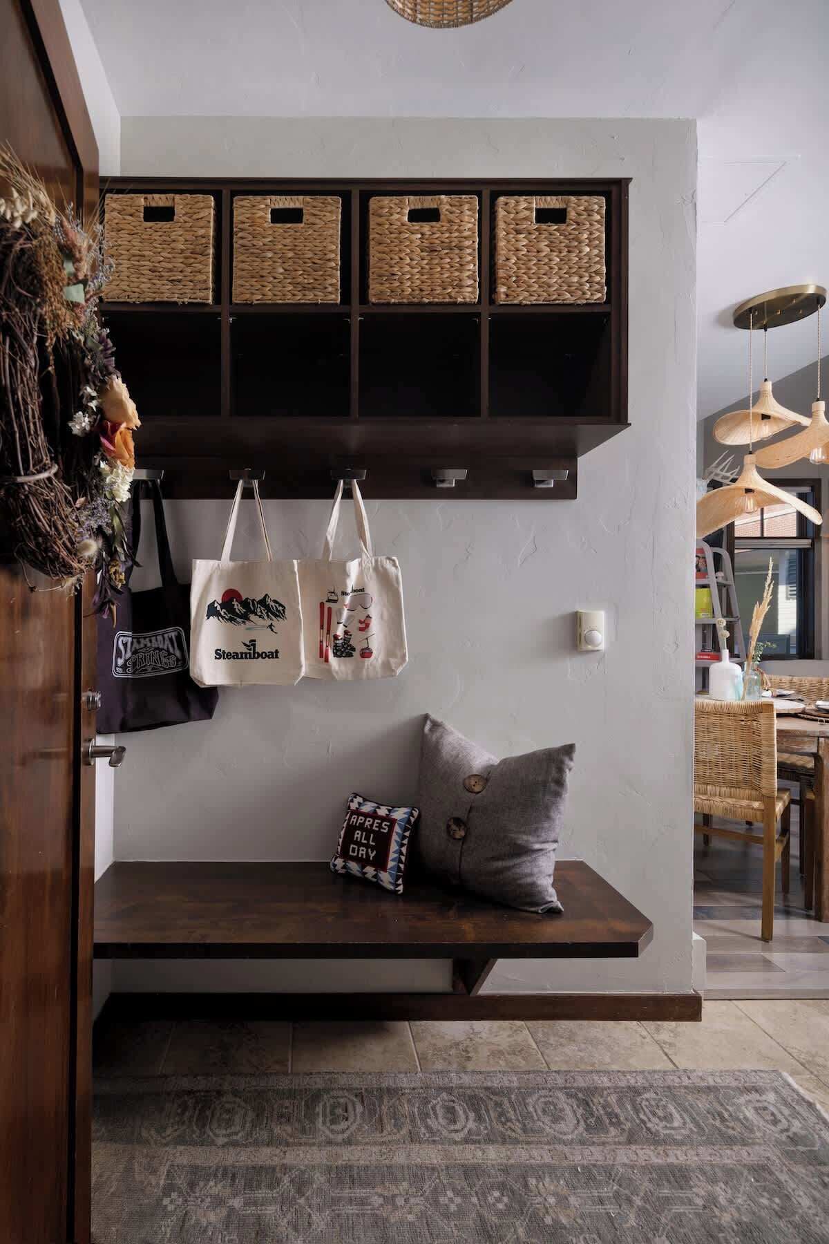A cozy seating area with a bench, a wall-mounted basket shelf, and a hanging light fixture.