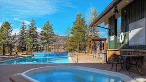 Zona de piscina con jacuzzi, pérgola de madera y mobiliario exterior.