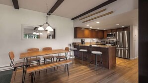 Una cocina moderna con electrodomésticos de acero inoxidable, una mesa de comedor de madera con taburetes altos y una isla grande con asientos tipo bar.