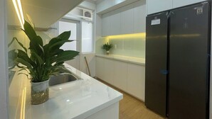 A modern kitchen with white cabinets, a black refrigerator, and a potted plant on the counter. - Nam Son Luxstay SG (Ho Chi Minh City)